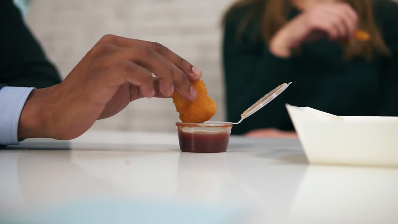 Close Up view of young african american hand dips chicken nugget in sauce during lunch at work in Slow Motion