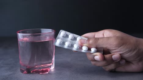 hand holding a blister pack of pills with a glass of water