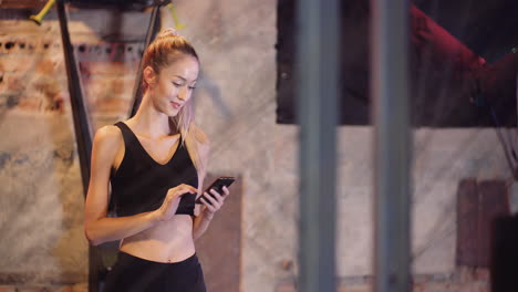 Schöne-Junge-Sportliche-Frau-Mit-Handy-Während-Der-Pause-Im-Fitnessstudio