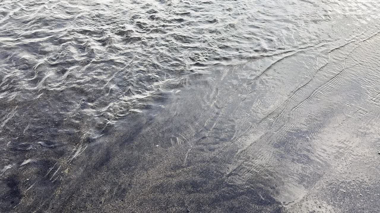 Clear Water Flowing Over Dark Sand on a Beach