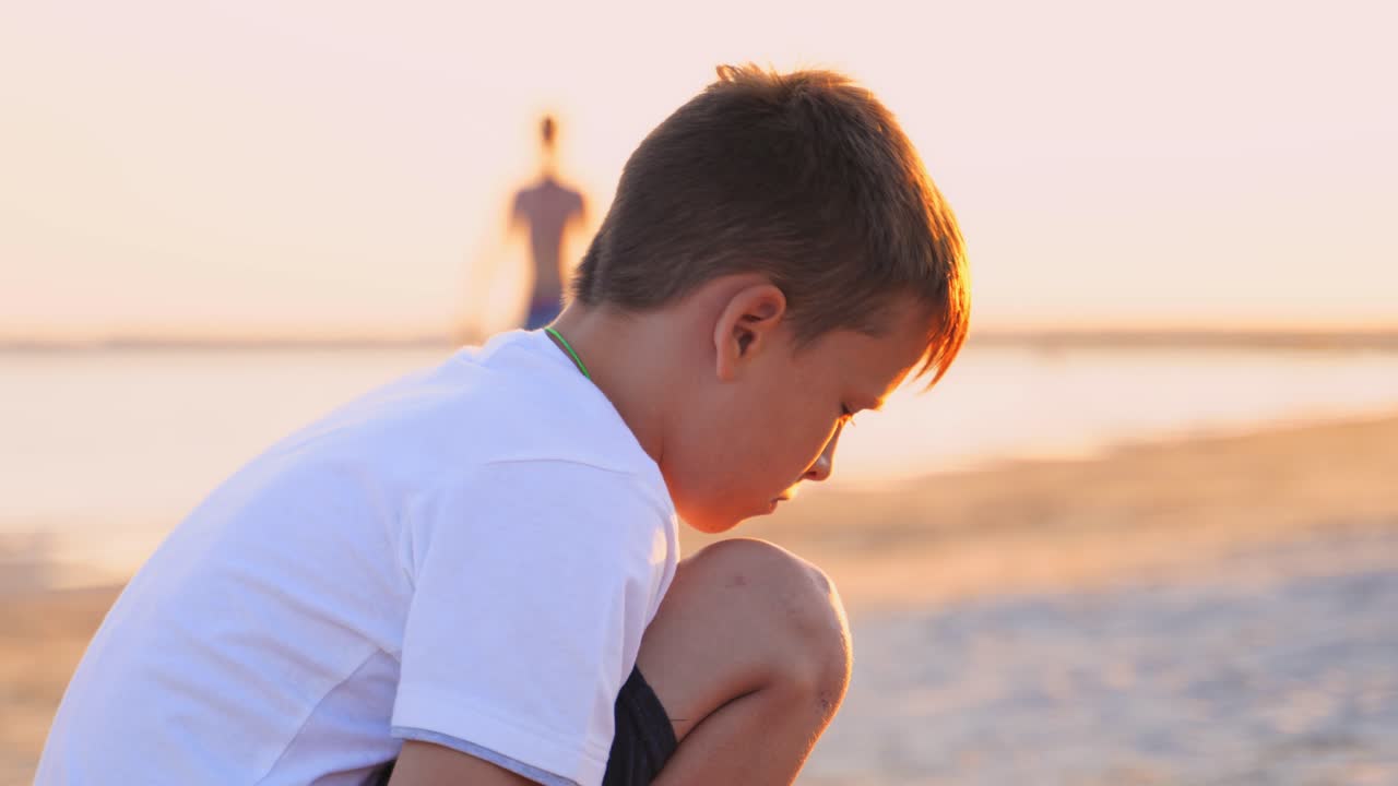 Side view of a boy in the sea shore. Boy is sitting on the sand beach in the evening at sunset. Close-up. Summer vacation.
