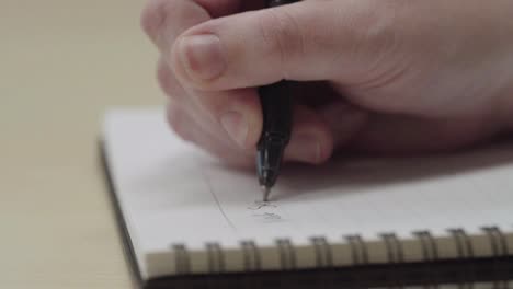 close up of anonymous person's hands writing on a notebook with a pen in slow motion