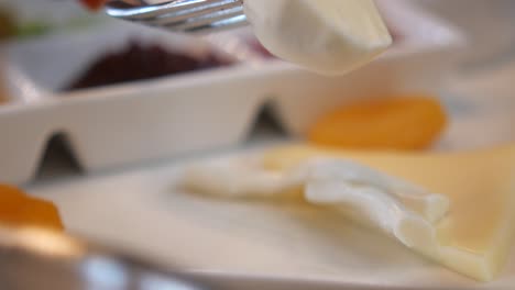 un primer plano de un tenedor recogiendo un pedazo de queso de un plato de desayuno