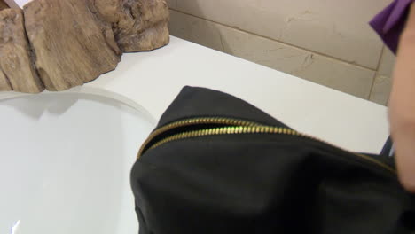 person opening a black makeup bag in a bathroom