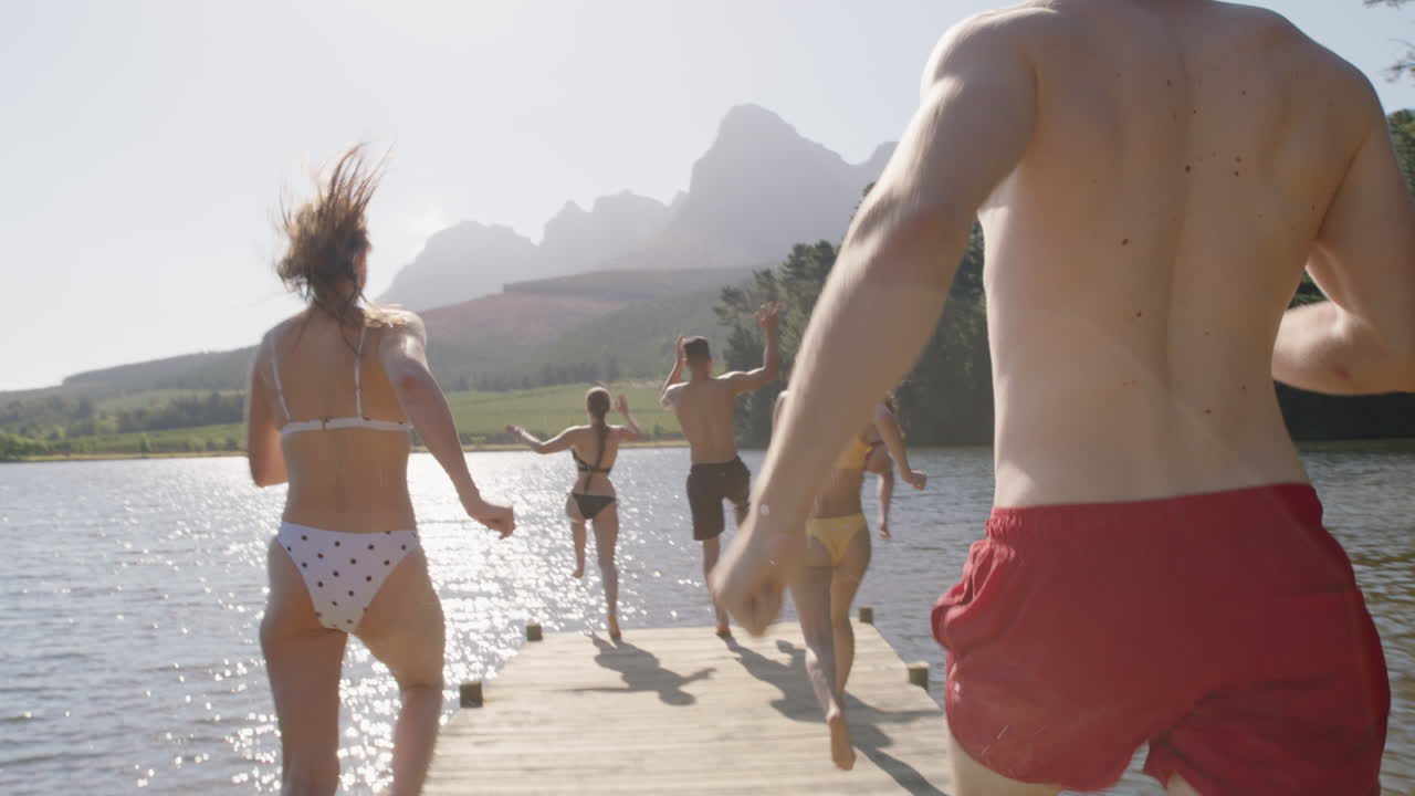 группа друзей прыгает в озеро, плясает в воде, веселится, наслаждается летним отдыхом.