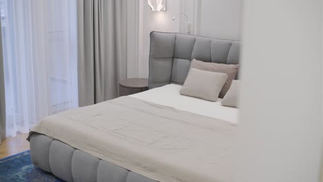 elegant bedroom setting with a gray tufted headboard, beige linen bedding, and a neutral color palette, accentuated by soft lighting and sheer curtains.