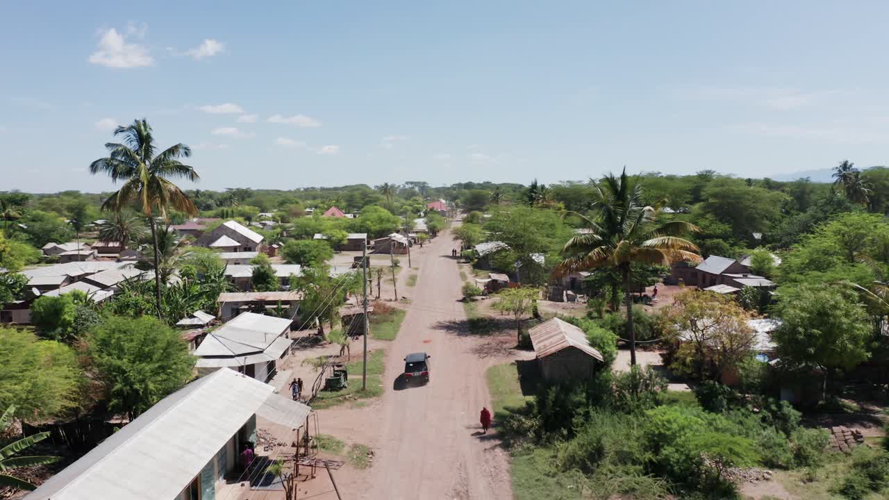 Aerial drone shot flying forward following a van in a little village next to Lake Manyara, Tanzania. Clear blue sky