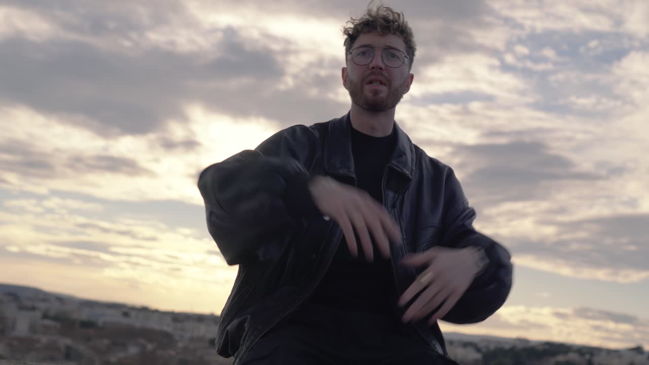 Man rapping passionately outdoors, performing hip-hop moves against a dramatic cloudy sky. Captures the raw energy and expressive power of street-style music and urban culture.