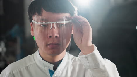 close-up of chinese student in lab coat adjusting protective glass in an automotive workshop, focused expression, bright workshop lighting illuminating background