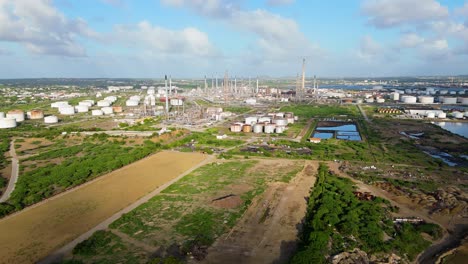 pan de camiones aéreos por encima de espacio verde de hierba vacía con estacas de llamaradas de refinería de petróleo en la distancia