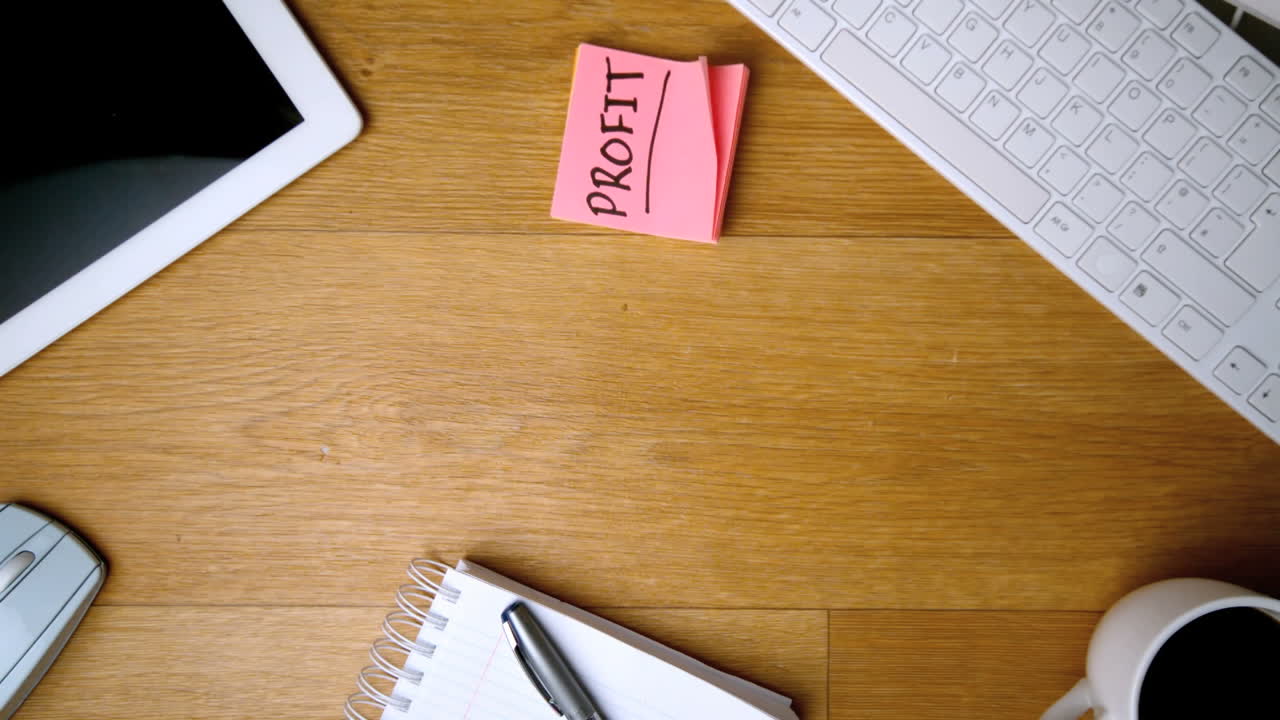 Pink sticky notes with profit written in bold falling on office desk