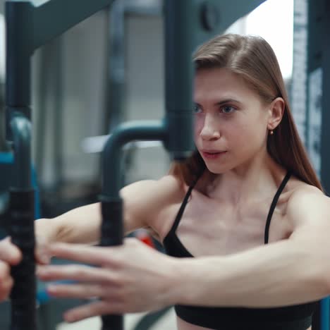 A beautiful girl with her strong arms performs an exercise on a simulator to strengthen the pectoral muscles in a fitness club. Close-up. Blurred Background