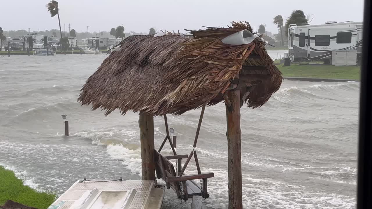 Hurricane conditions with strong winds and high waves battering a coastal area with an RV park and tiki hut