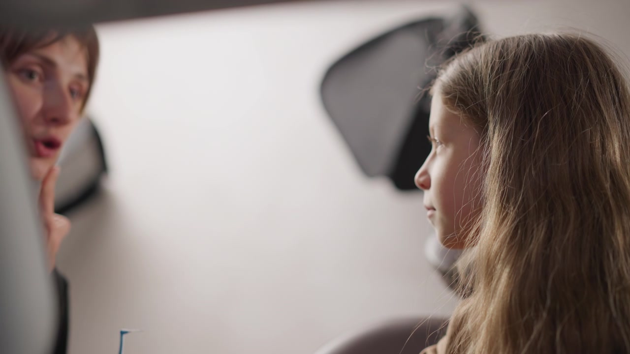 Close up of young girl sitting in orthodontic consultation room while her mother explains dental care. scene features soft lighting and minimal camera movement focusing on interaction
