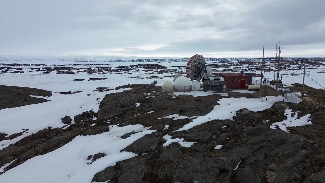 Drone-sporingsopptak av parabolantenner med utsikt over steinete tundraåser under vårens snøsmelting i Iqaluit.