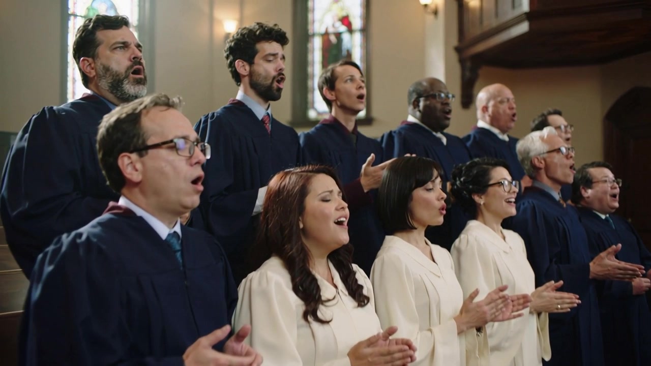 Coro che canta e inizia un inno dopo un segnale, esprimendo devozione in una chiesa con vetrate colorate e vesti.