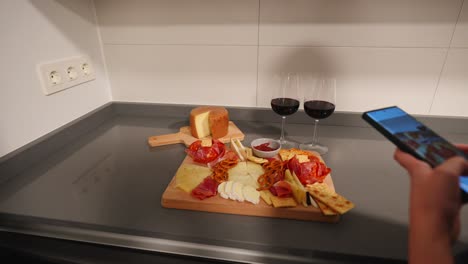 Mujer-Tomando-Fotografías-De-Una-Tabla-De-Quesos-Y-Vino-Tinto-Con-Un-Teléfono.