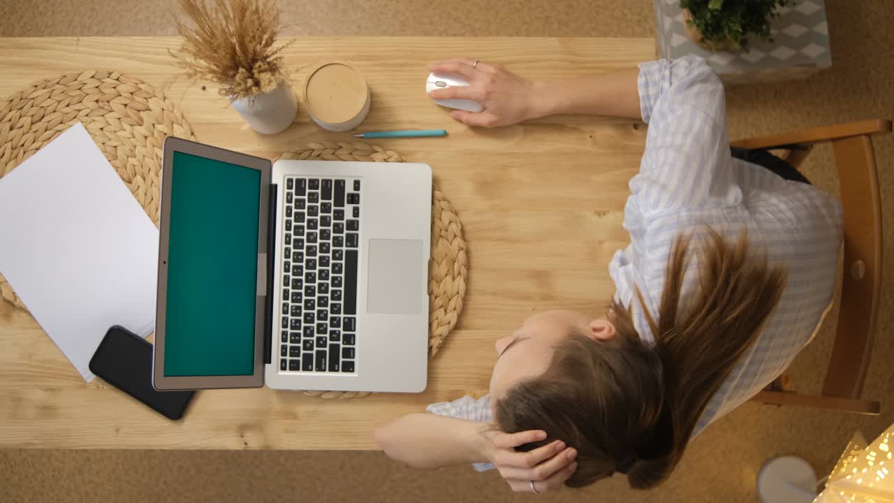 The concept of remote work at home. The girl is sitting in pejama at a table with a laptop and working. Green monitor screen. Paper phone mouse Top view