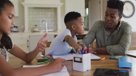 african american father, daugher and son sitting at kitchen table doing homework