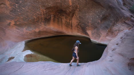 young female hiker walking on sandstone cliff above rainwater pond in wilderness of utah, st