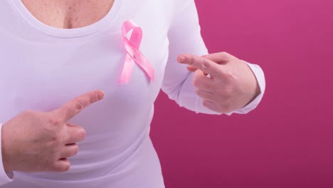 Video-of-midsection-of-caucasian-woman-wearing-pink-cancer-awareness-ribbon,-with-pink-background