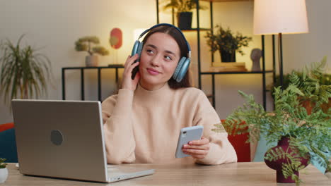 Happy-woman-in-wireless-headphones-relaxing-listening-favorite-rock-n-roll-music-sits-at-home-table