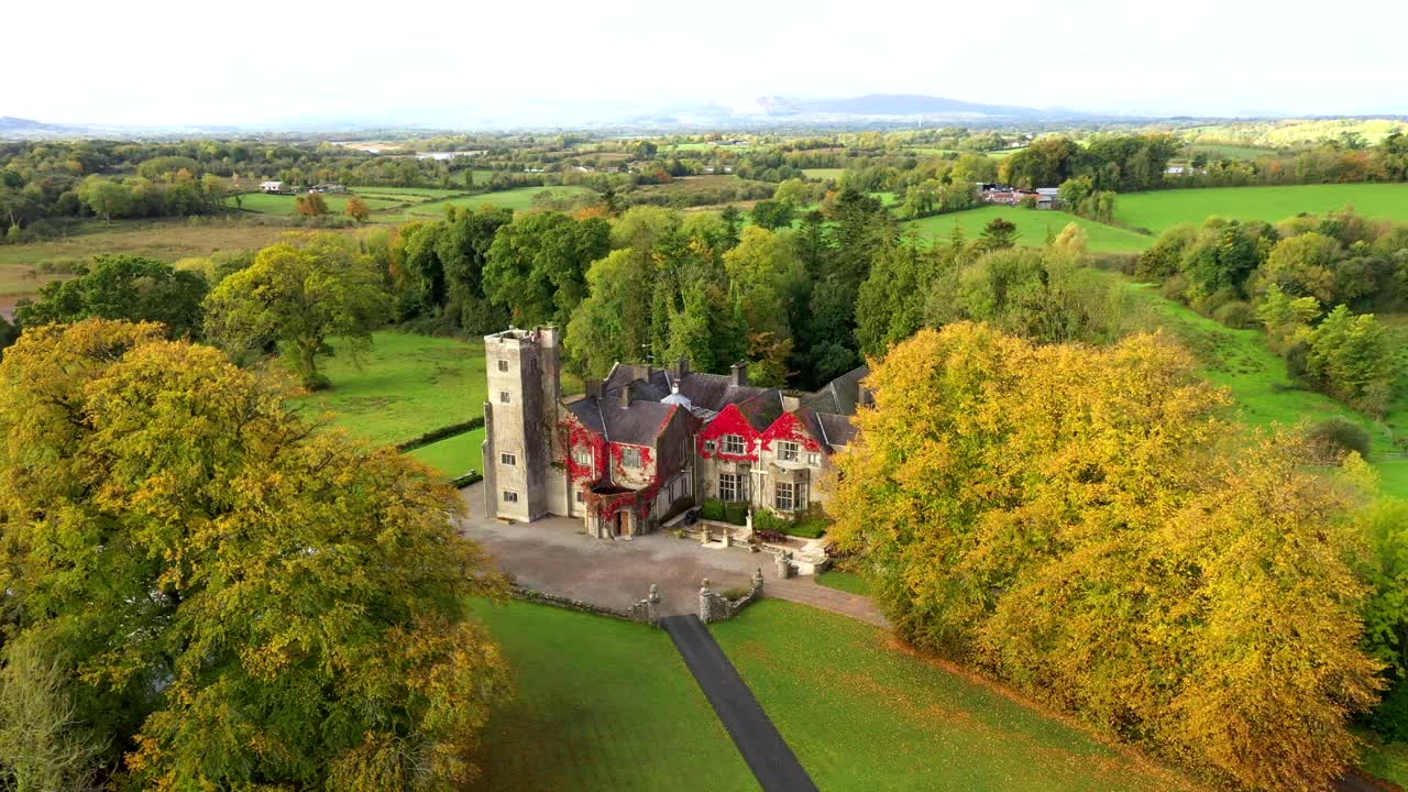 Drone tracking reveal over vibrant castle garden with fall trees and wide landscape in Northern Ireland