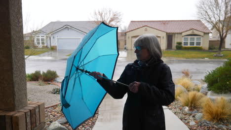 una bonita mujer de mediana edad caminando fuera de la lluvia de invierno y guardando su paraguas azul en un barrio a cámara lenta