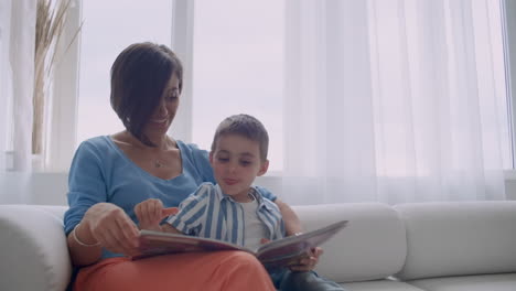 madre feliz y hijo pequeño leyendo un libro por la mañana juntos en la sala de estar en casa. concepto de actividad familiar.