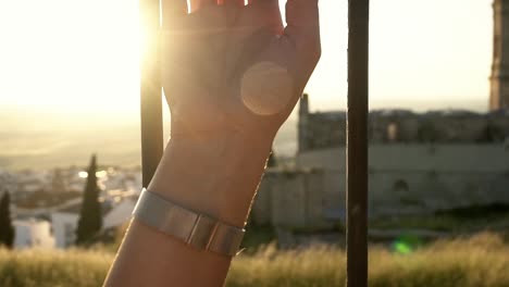 tilting shot of a model arm holding onto a fence with a church in the background during sunset