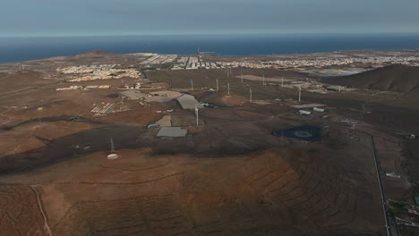 aerial perspective revealing roque aguayro landmark with spinning wind turbines against golden sunset lighting over gran canaria agricultural landscape