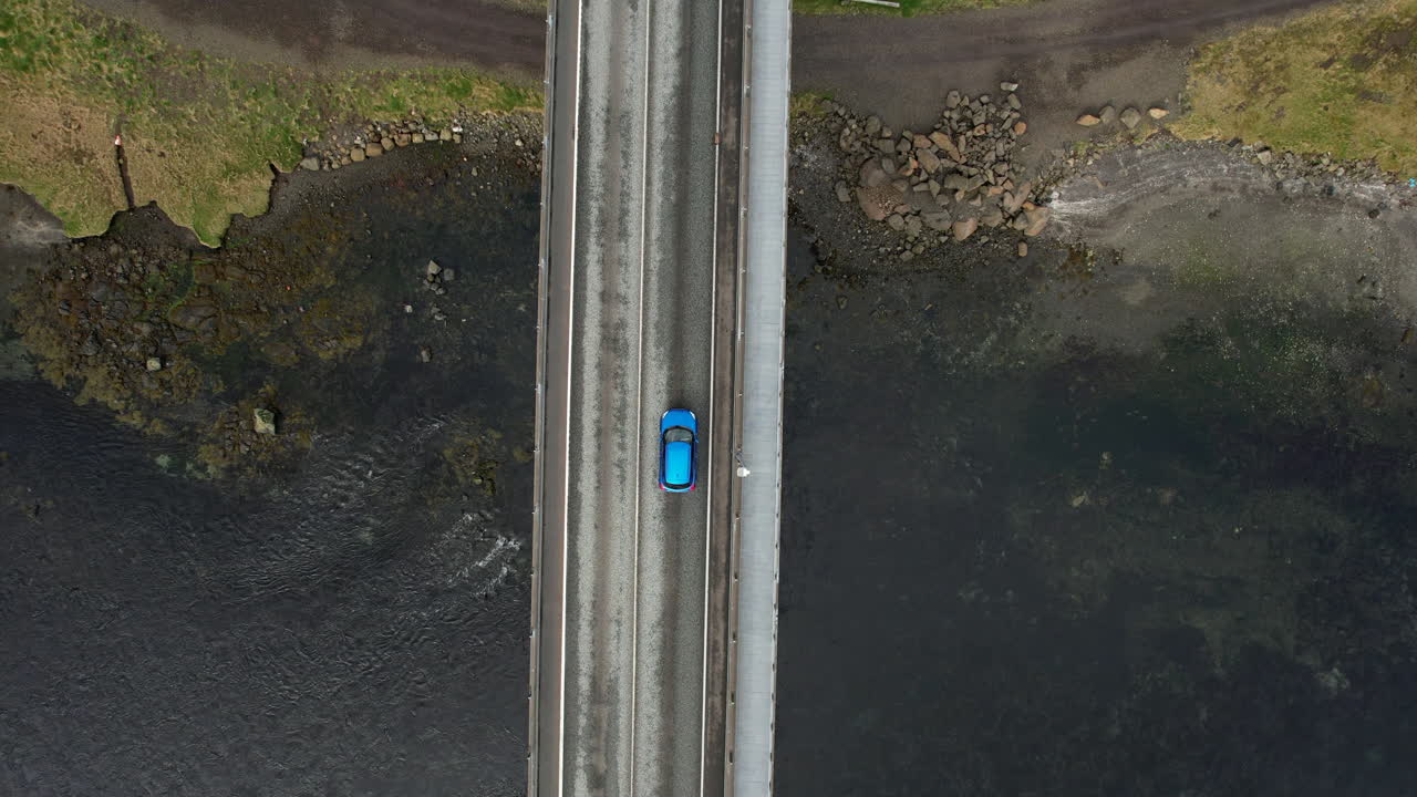 Aerial top down view of a car driving over a bridge connecting two islands in the Faroe Islands