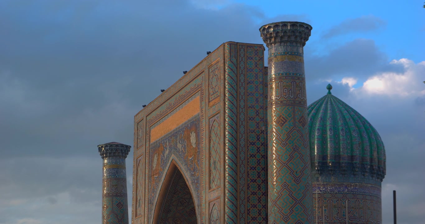 Nahaufnahme der Registan-Minarette, des gekachelten Portals und der türkisfarbenen Kuppel unter blauem, bewölktem Himmel in Samarkand, Usbekistan. Historische islamische Architektur, zentralasiatisches Kulturerbe, Reise- und Tourismuskonzept.