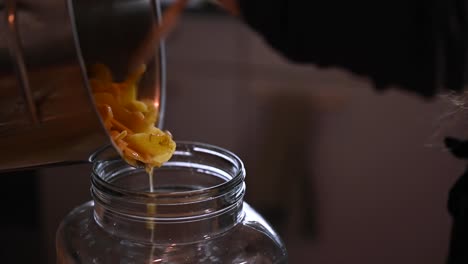 Close-up-shot-of-person-pouring-freshly-made-ginger-drink-with-fresh-ginger-slices-into-glass-container