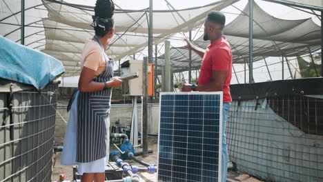 african american diverse man and woman discussing solar panel installation in greenhouse
