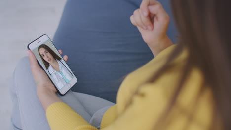 A-woman-lying-on-the-couch-talking-to-a-woman-doctor-on-video-using-a-smartphone.-Remote-medical-consultation-with-a-doctor-via-mobile-phone