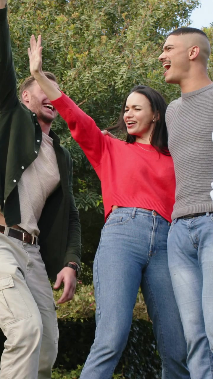 Video verticale: Amici con maglione che salutano e si muovono nel parco all'arrivo di un uomo con giacca verde.