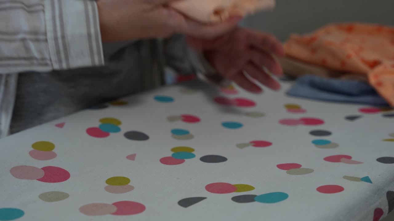 Female hands fold orange baby bodysuit on ironing board in closeup