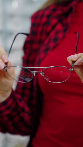 stylish eyeglasses in woman's hands. female buyer holding new spectacles in the optical store. close-up. vertical video