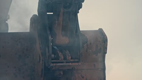 close-up of a large excavator arm with a bucket digging into the earth, creating dust and smoke.