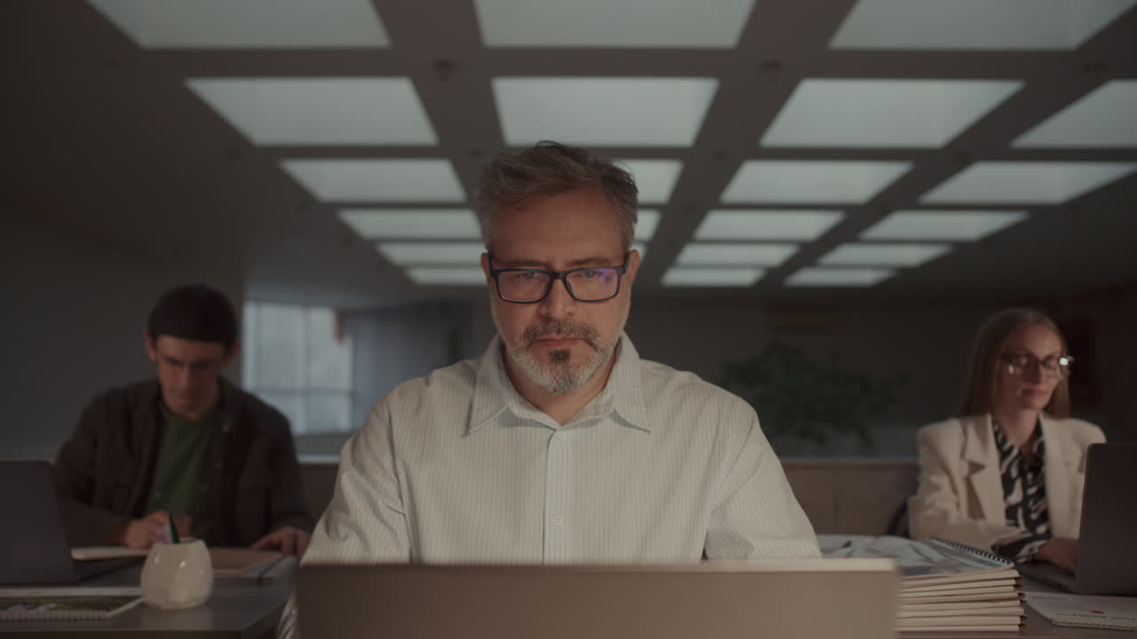 Focused Man Working on Laptop at Desk with Business Team Around