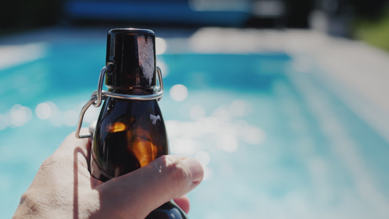 un hombre sostiene una botella de cerveza en su mano, se relaja junto a la piscina en un día caluroso