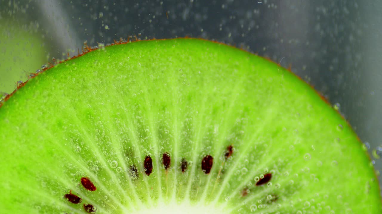 A piece of green kiwi under water with air bubbles.