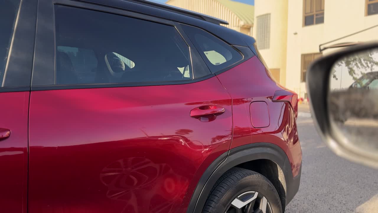 Primo piano di un SUV rosso parcheggiato su una strada residenziale di giorno, inquadrato accanto a uno specchietto laterale, che mostra i dettagli esterni del veicolo, il contesto di parcheggio urbano e il design automobilistico moderno