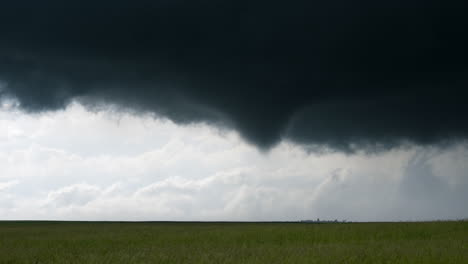 tornado slowly touches down from dramatic dark storm base in open farm land