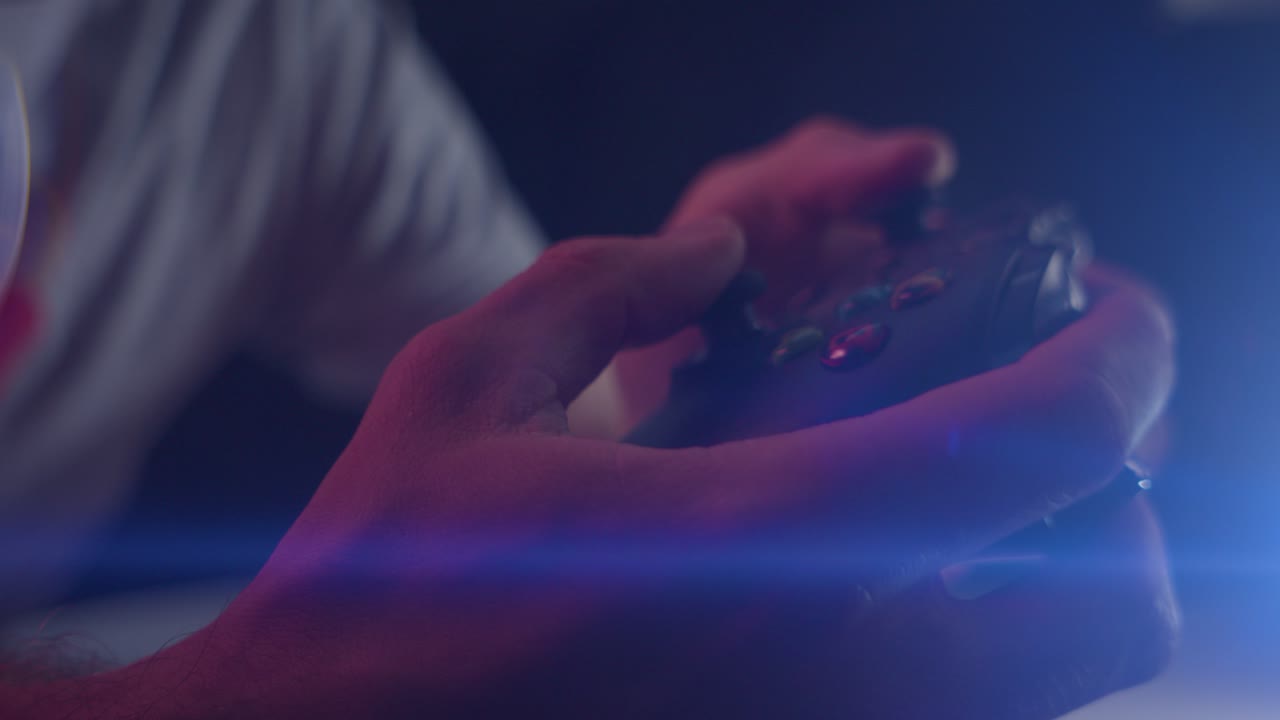 Giocare ai videogiochi in una stanza buia con un bagliore anamorfico dell'obiettivo sui pulsanti di un controller premuti rapidamente, in primo piano