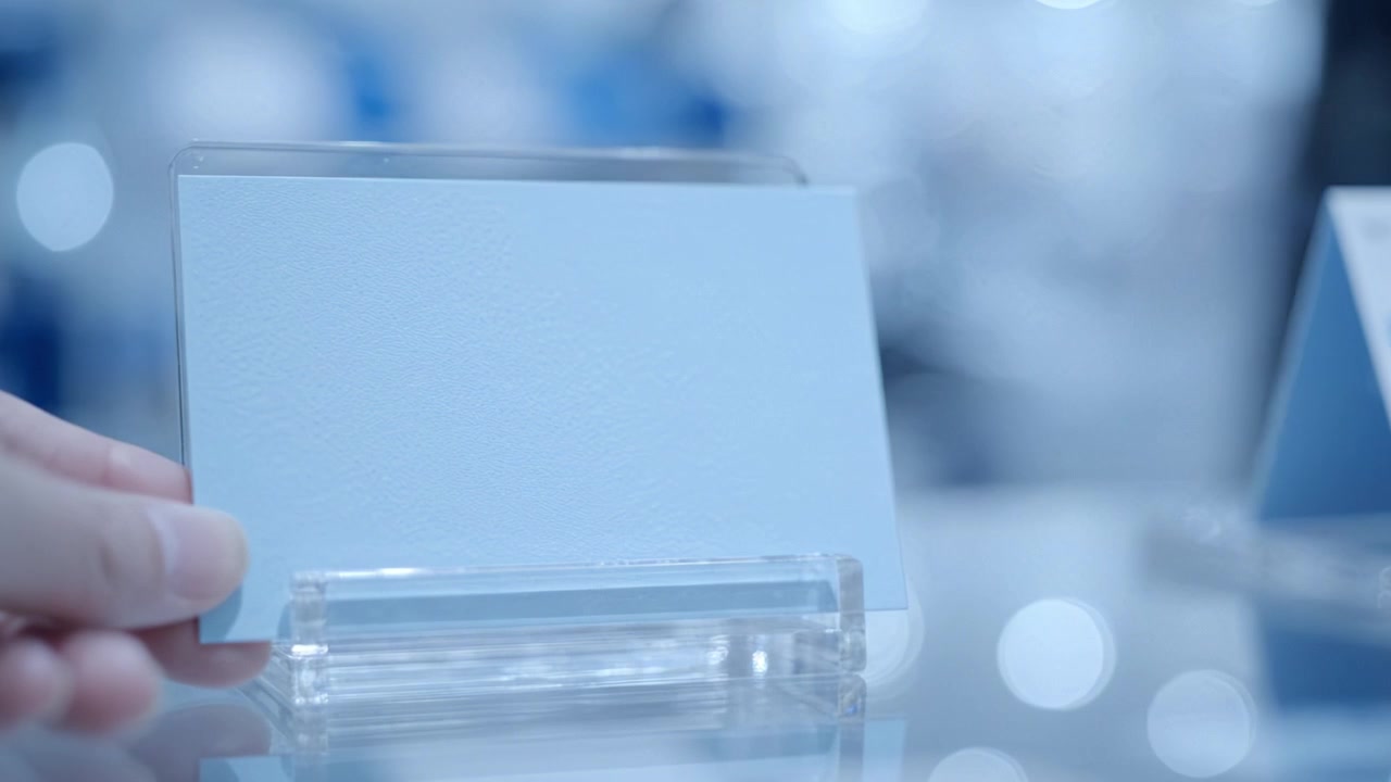 Una mano che tiene un biglietto bianco in un supporto trasparente su uno sfondo leggermente sfocato, creando un ambiente di presentazione elegante e minimalista.