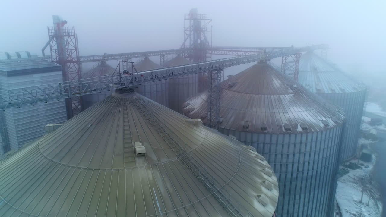 The rounded tops of the silo tanks. Drone shot over the modern grain elevators on foggy weather. Impressive granary constructions from aerial perspective.