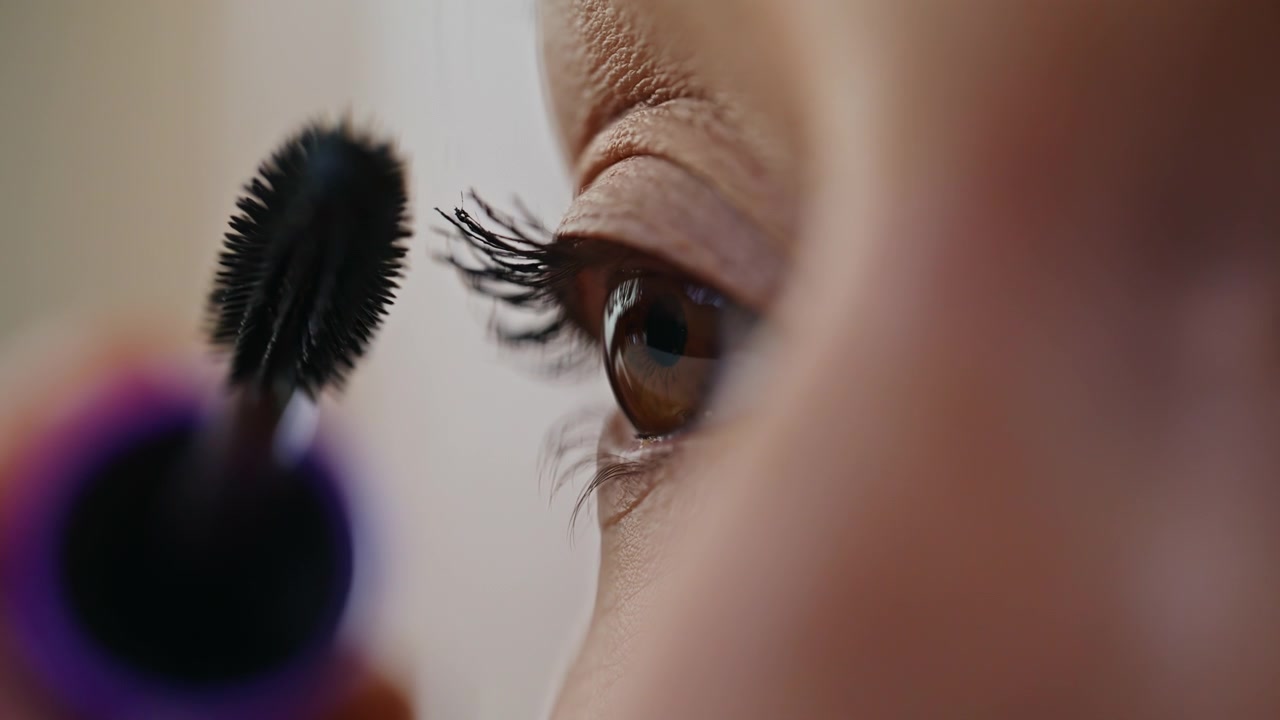 Primo piano di una donna che si trucca le ciglia usando un pennello cosmetico. Giovane donna che applica il mascara.