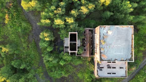 drone looking down on and flying away from an abandoned overgrown coal mine